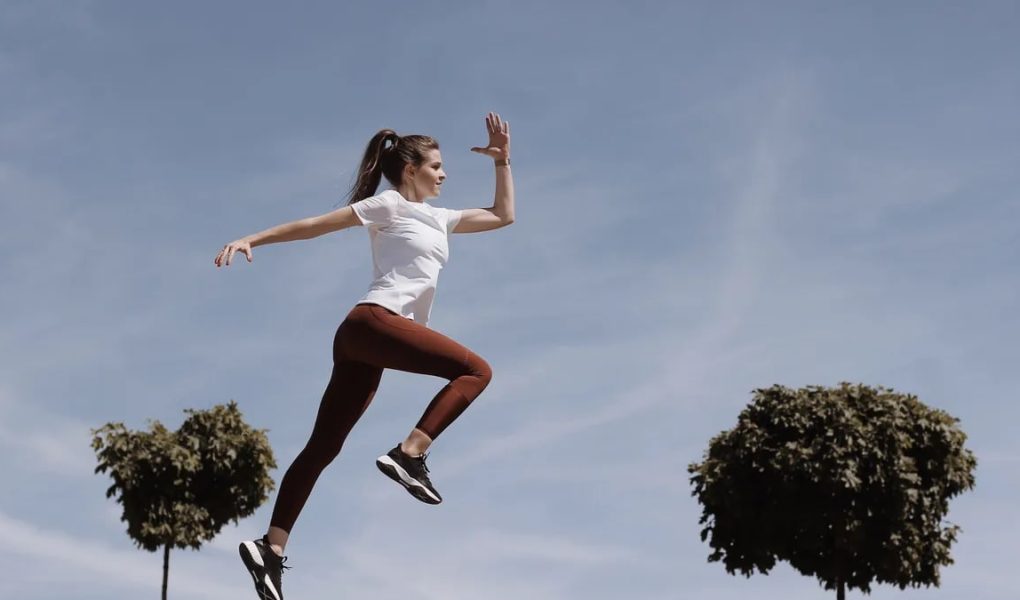 Athletic woman in action jump against a blue sky background. Captures fitness in motion.