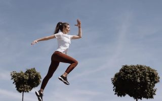 Athletic woman in action jump against a blue sky background. Captures fitness in motion.